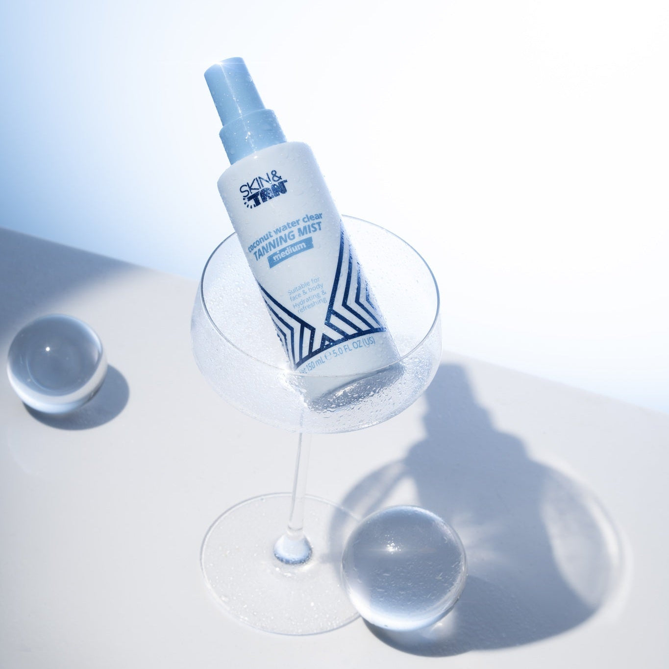 Skin & Tan Coconut Water Tanning Mist beside water on a blue studio set