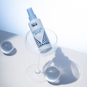 Skin & Tan Coconut Water Tanning Mist beside water on a blue studio set